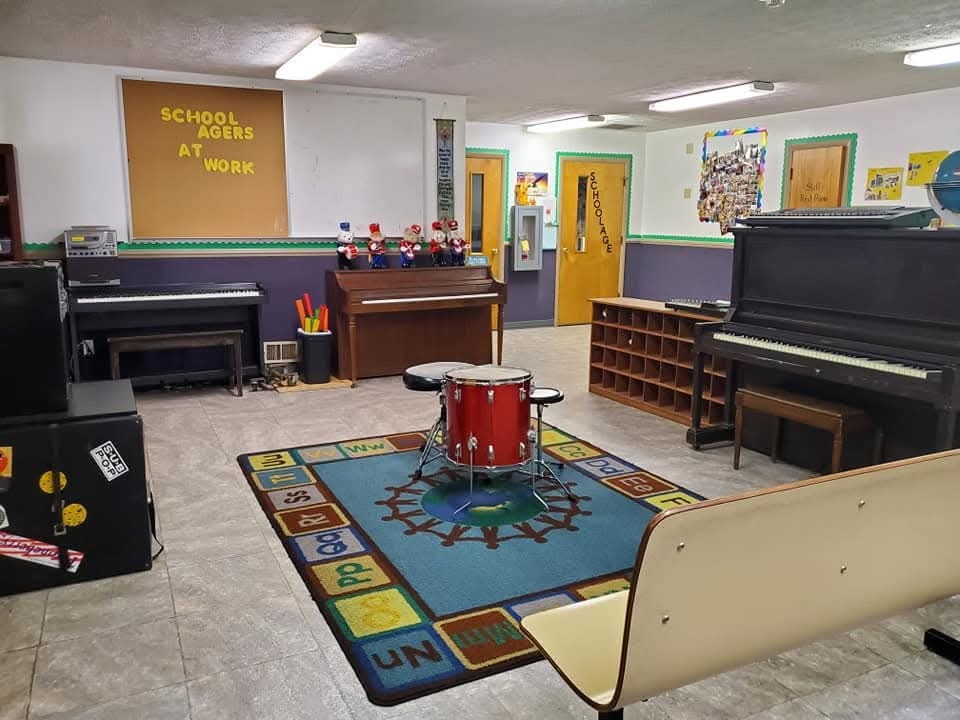 School-Age music room with pianos, drums, and a 'School Agers at Work' display