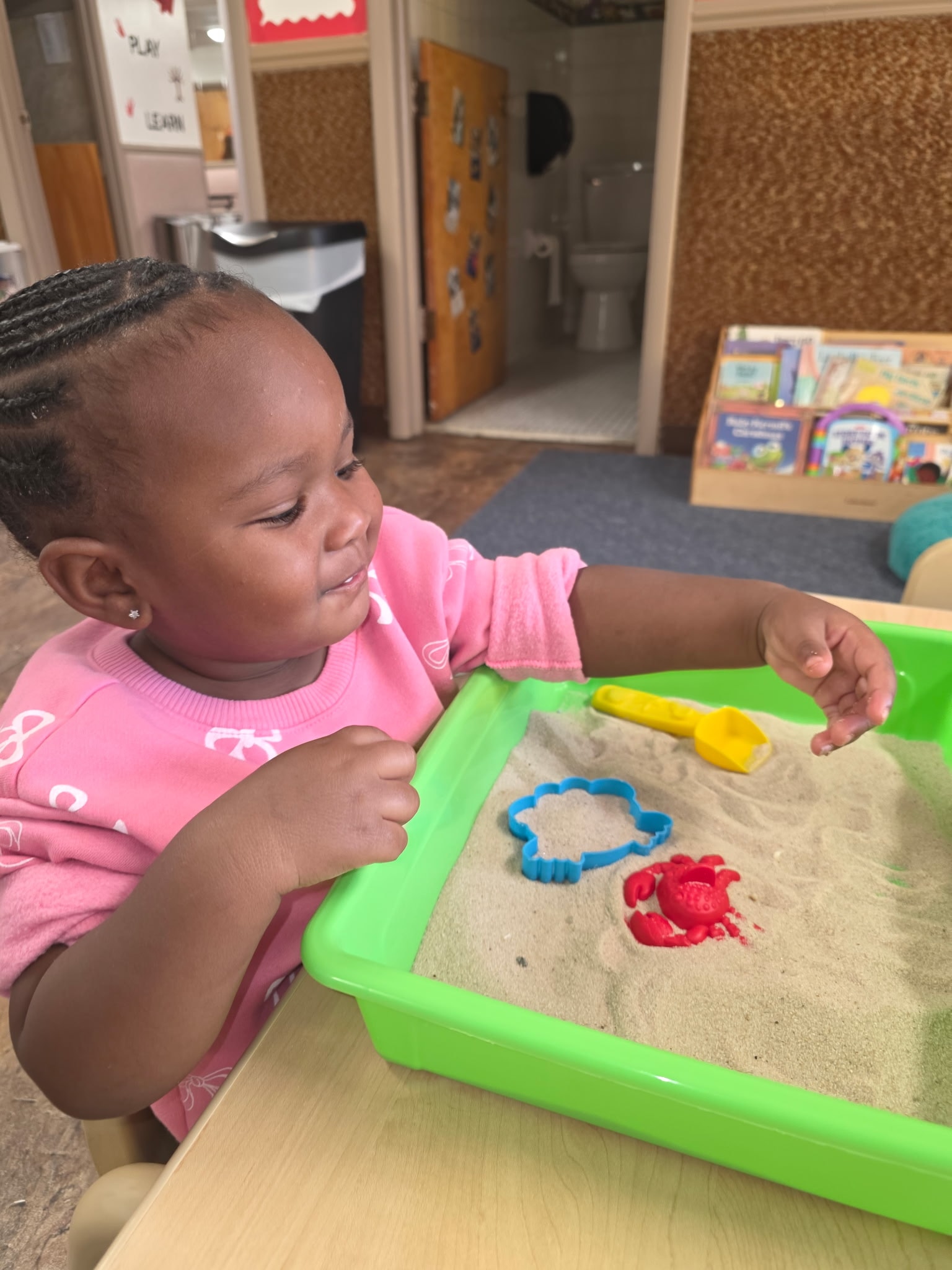 Baby girl playing in the sand table with colorful molds and scoops