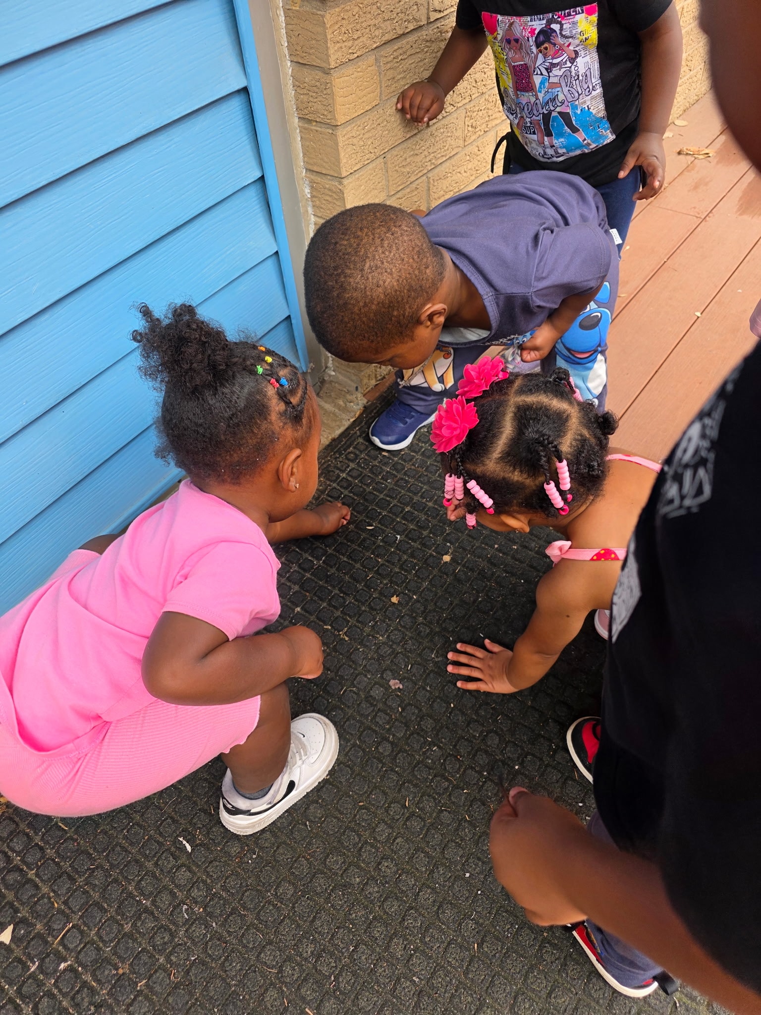Group of young children crouching together outdoors curiously examining something on the ground