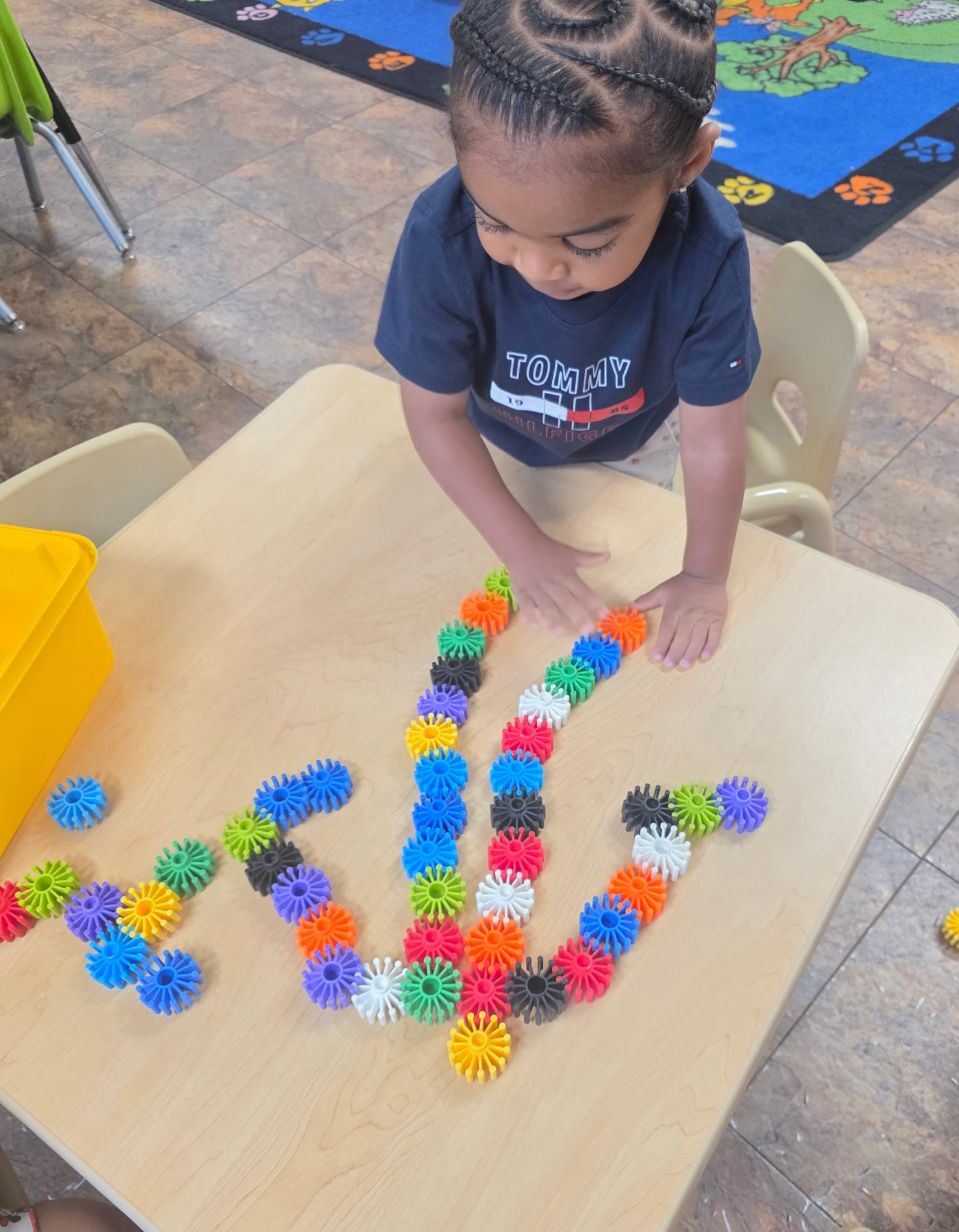Toddler carefully arranging colorful interlocking gear pieces into a pattern on a classroom table