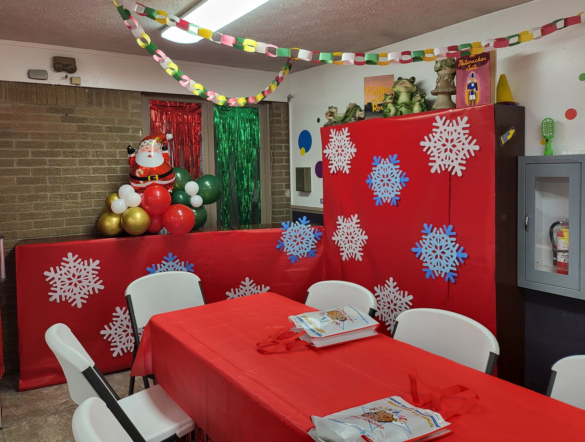 Holiday party room decorated with snowflake cutouts, Santa balloon, and red tablecloths