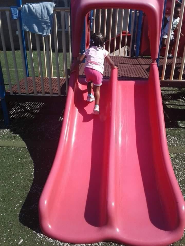 Child climbing up the pink slide on the outdoor playground