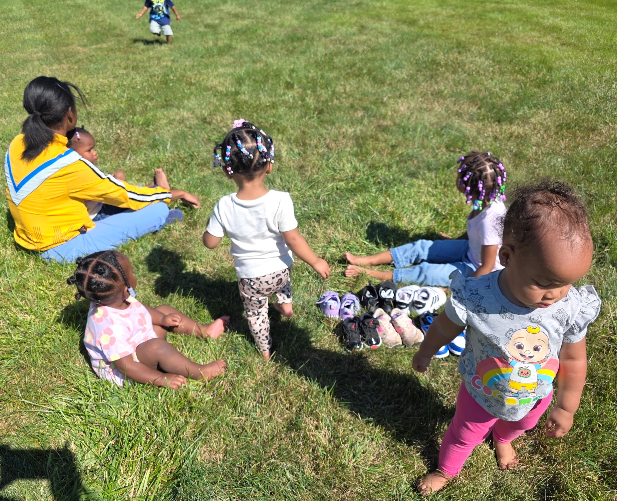 Teacher sitting on the grass with toddlers enjoying outdoor playtime on a sunny day
