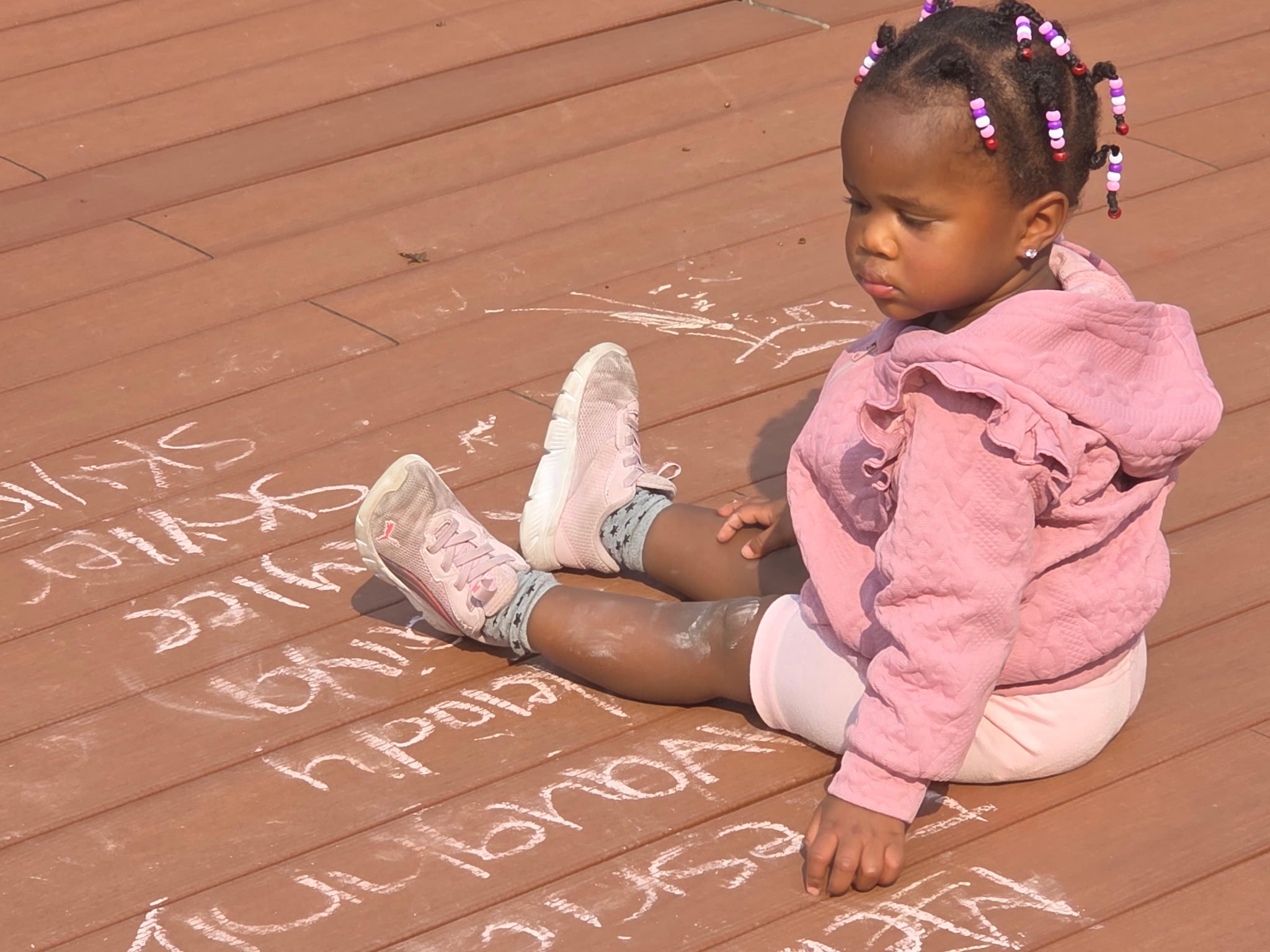 Young girl in a pink hoodie sitting on the outdoor deck surrounded by chalk writing