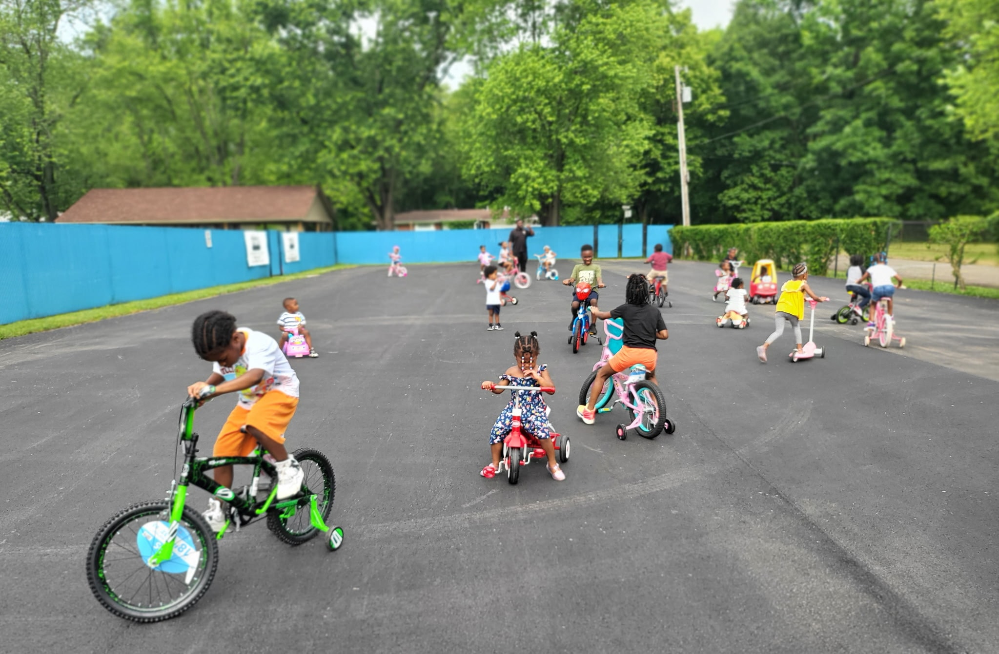 Children riding bikes, tricycles, and scooters together in the outdoor play area on a sunny day
