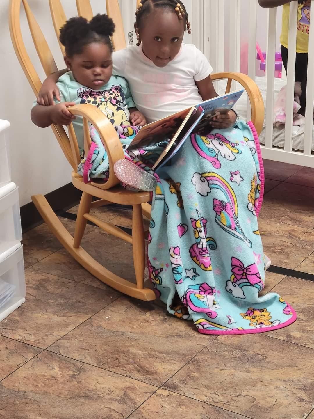 Two girls snuggled together in a rocking chair sharing a storybook